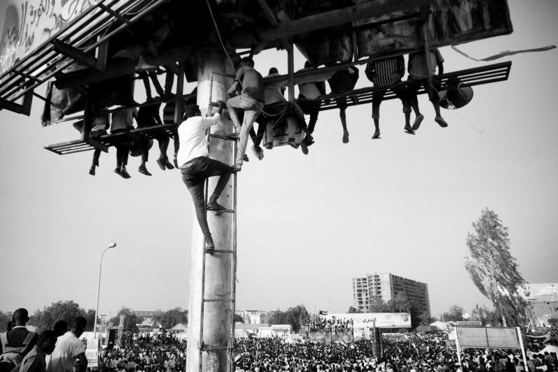 Ahmed Ano, Des civils escaladent d’énormes panneaux publicitaires pour crier « Liberté, paix et justice ». Sit-in, quartier général militaire, Khartoum, 19 avril 2019.