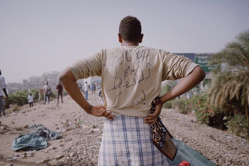 Muhammad Salah. Un manifestant dont l'inscription au dos de sa chemise signifie « Un révolutionnaire de Kalakla, que la dictature tombe ! » ; il se tient sur la ligne ferroviaire centrale de Khartoum qui faisait partie de la zone de sit-in du QG de l'a