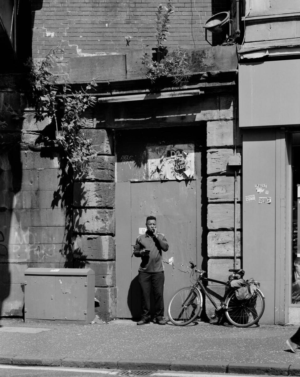 Camille Fallet, Man waiting for a delivery in front of an old entrance along railway bridge, Dubarton Road, [Un livreur attend adossé à une vieille porte d’entrée le long du pont de chemin de fer sur Dubarton Road], Glasgow, 2019.
